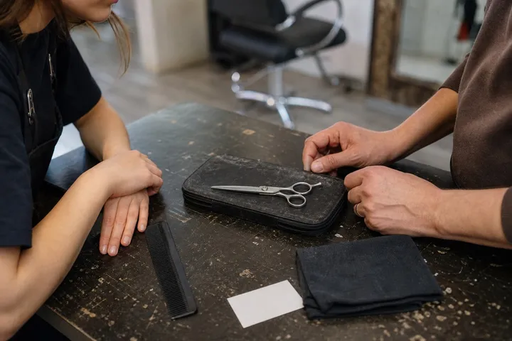 Two people discuss a cutting scissor resting on a case at a salon bench.