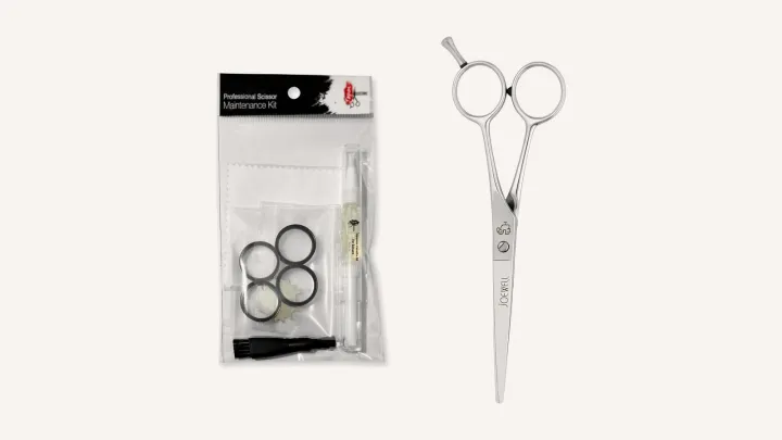 A scissor maintenance kit with oil, cloth, brush, finger inserts and tension key beside a Joewell Classic cutting scissor.