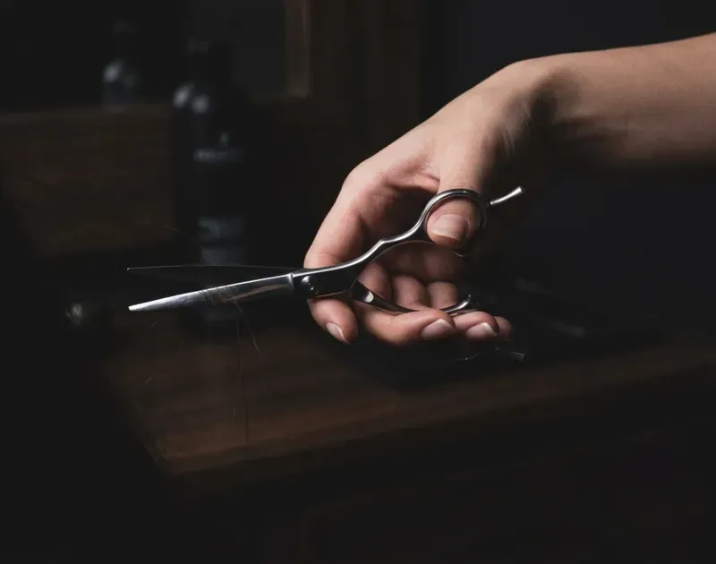 Hand holding hair scissors over a dark table