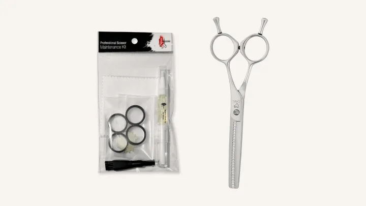 A scissor maintenance kit with oil, cloth, brush, finger inserts and tension key beside a Joewell E40 thinning scissor.