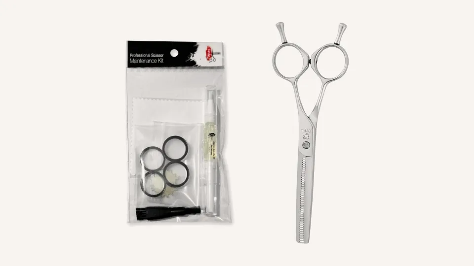 A scissor maintenance kit with oil, cloth, brush, finger inserts and tension key beside a Joewell E40 thinning scissor.