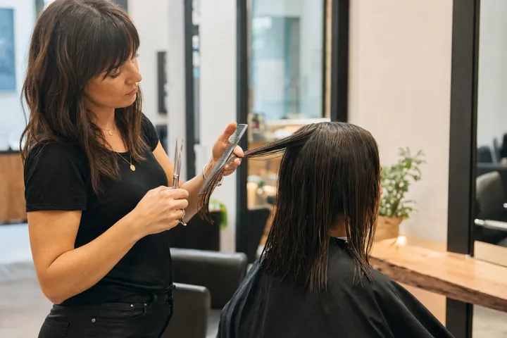 A stylist holding a comb and shear while lifting a section of wet hair.